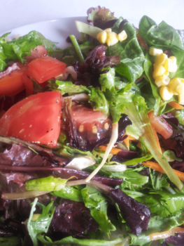 Mixed salad with leafy greens, tomato slices, shredded carrots, and corn kernels on a white plate.