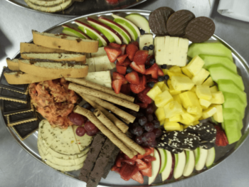 Platter with assorted cheeses, fruits, cookies, crackers, and chocolate arranged on a metal tray.