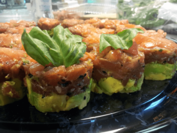 Small stacks of diced avocado and tuna topped with basil leaves, arranged on a black platter.