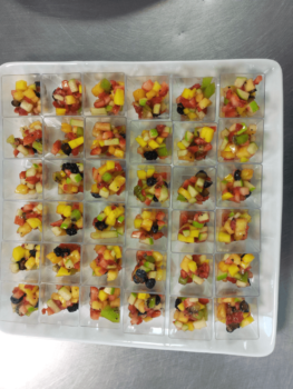 Tray with 35 small cups of diced fruit salad, arranged in a rectangular grid on a white platter.