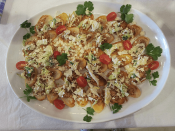 Oval platter with mini tostadas topped with cheese, lettuce, tomatoes, and garnished with cilantro on a white tablecloth.