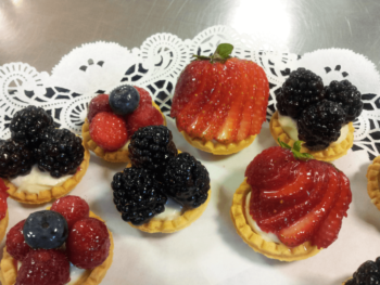 Assorted fruit tarts with blackberries, strawberries, raspberries, and blueberries on a doily-lined tray.