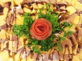 Sliced melon and prosciutto arranged with parsley and a tomato rose, drizzled with balsamic glaze.