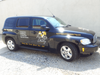 Black Figs & Honey Catering car with company logo, service list, phone number, and website on the side, parked outside.