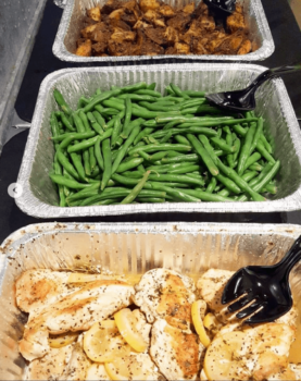 Three trays with roasted chicken and lemon slices, green beans, and seasoned beef, each with a serving spoon.