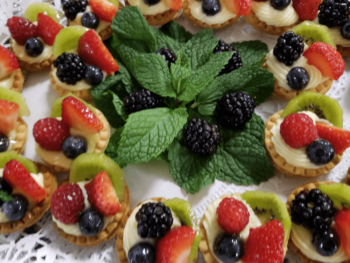 Mini fruit tarts with cream filling are arranged around fresh mint leaves on a lace doily.