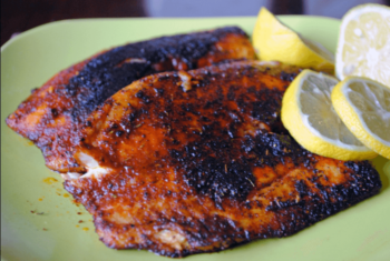 Two pieces of blackened fish fillet on a plate, garnished with lemon wedges.