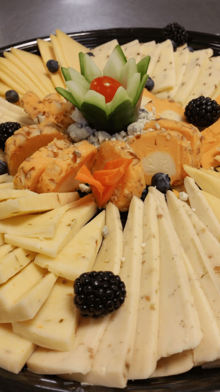 Assorted sliced cheeses arranged in a circular pattern with blackberries and a decorative vegetable garnish in the center.
