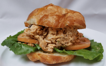 Chicken salad with lettuce and tomato on a croissant, served on a white plate with a white background.