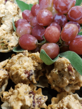 Red grapes with leafy greens, surrounded by creamy chicken salad in phyllo cups on a black platter.