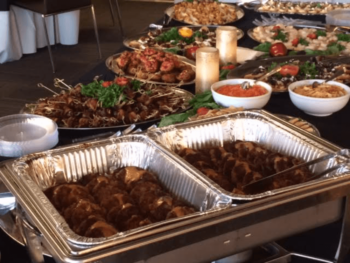 Buffet table with various hot and cold dishes, including meat, salads, dips, and decorative candles.