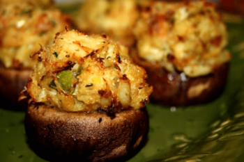 Three baked mushrooms stuffed with a golden, herbed breadcrumb and vegetable mixture are shown on a green plate.