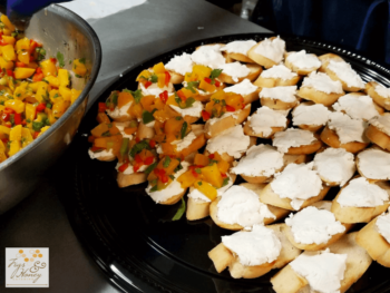 Platter of baguette slices topped with white cheese, some garnished with diced yellow and red peppers and herbs.