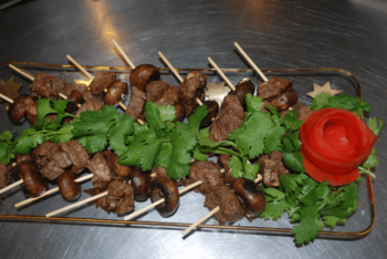 Skewers with grilled beef and mushrooms on a tray, garnished with cilantro and a carved tomato rose.