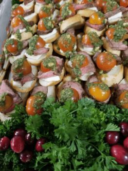Crostini topped with roast beef, mozzarella, cherry tomato halves, and pesto, garnished with parsley and cranberries.