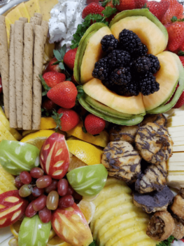 Assorted fresh fruit, cheese slices, cookies, and pastries arranged on a platter for serving.