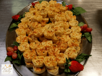 A platter of bite-sized, baked cheese appetizers garnished with fresh strawberries, grapes, and green leaves.