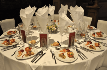 Round table set for a formal dinner with plated appetizers, drinks, menus, and neatly folded napkins.