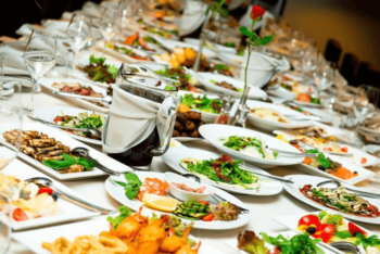 A long table set with plates of assorted food, salads, and drinks, ready for a banquet or large gathering.