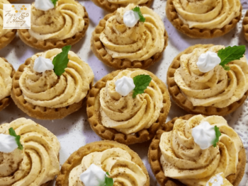 Mini tarts with swirled cream filling, a dollop of whipped topping, and mint leaves arranged on a tray.