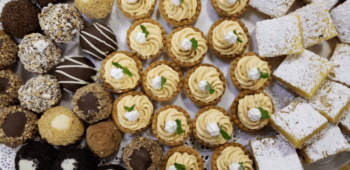 An assortment of bite-sized desserts, including tarts, lemon bars, and chocolate-covered treats, arranged on a tray.