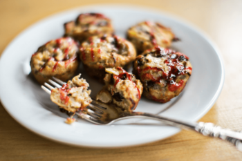 Six mini meatloaf muffins drizzled with ketchup are served on a white plate with a fork.