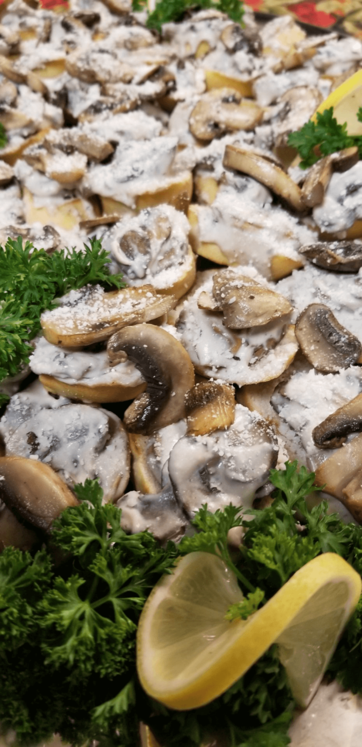 Sliced mushrooms in a creamy white sauce, garnished with fresh parsley and lemon wedges.