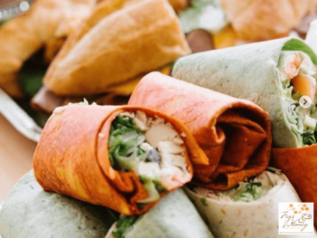 Assorted wraps with visible greens and chicken, stacked on a tray; logo for “Fig & Honey” appears in the corner.