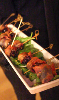 Staff holding plate of the hors d'oeuvres Bacon Wrapped Dates stuffed with Goat Cheese